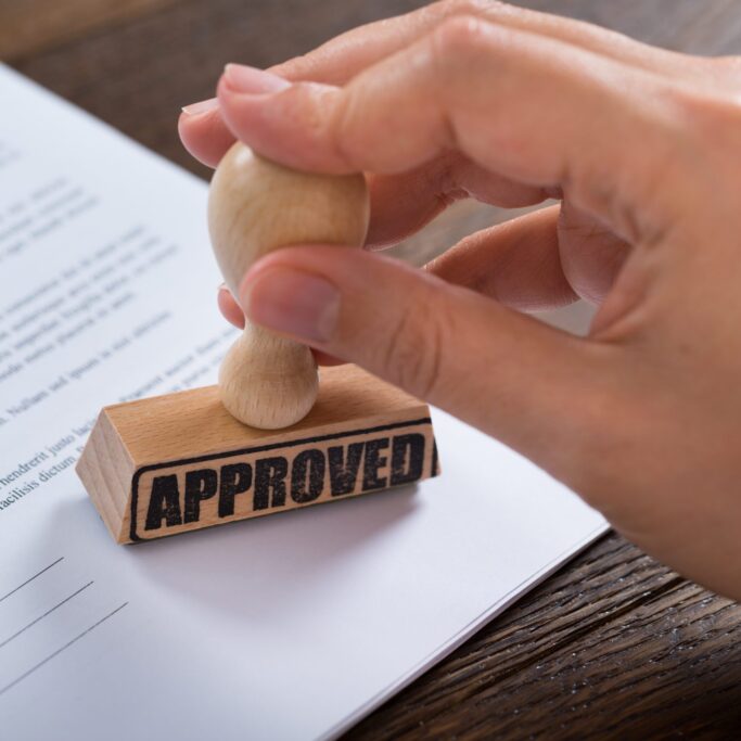 Close-up Of Person Hands Using Stamper On Document With The Text Approved